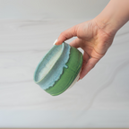A hand holds the Iguchi Deep Sea Clay Matcha Bowl, showcasing its green and blue Minoyaki pottery design against a softly blurred background.