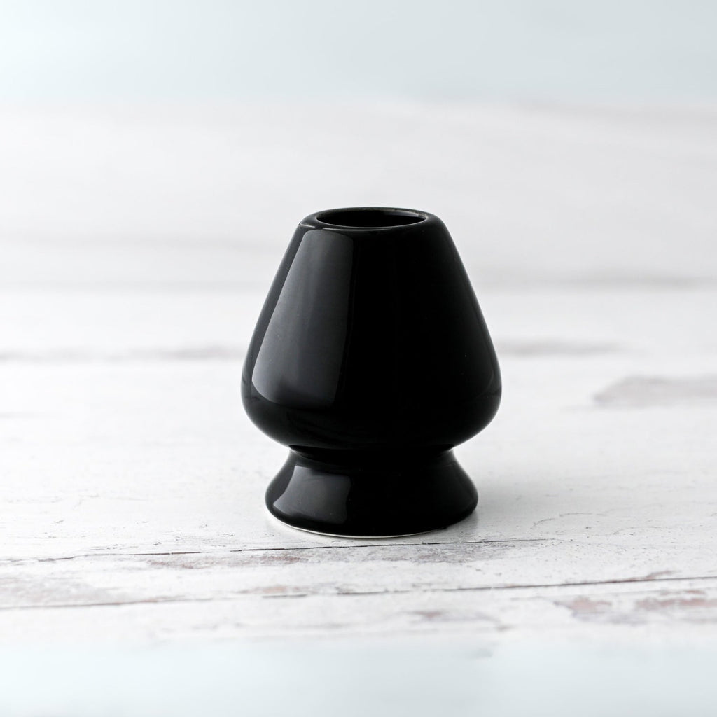 A Black Matcha Whisk Holder from the Bamboo Whisk Set, echoing a Japanese aesthetic, sits elegantly on a white wooden surface.
