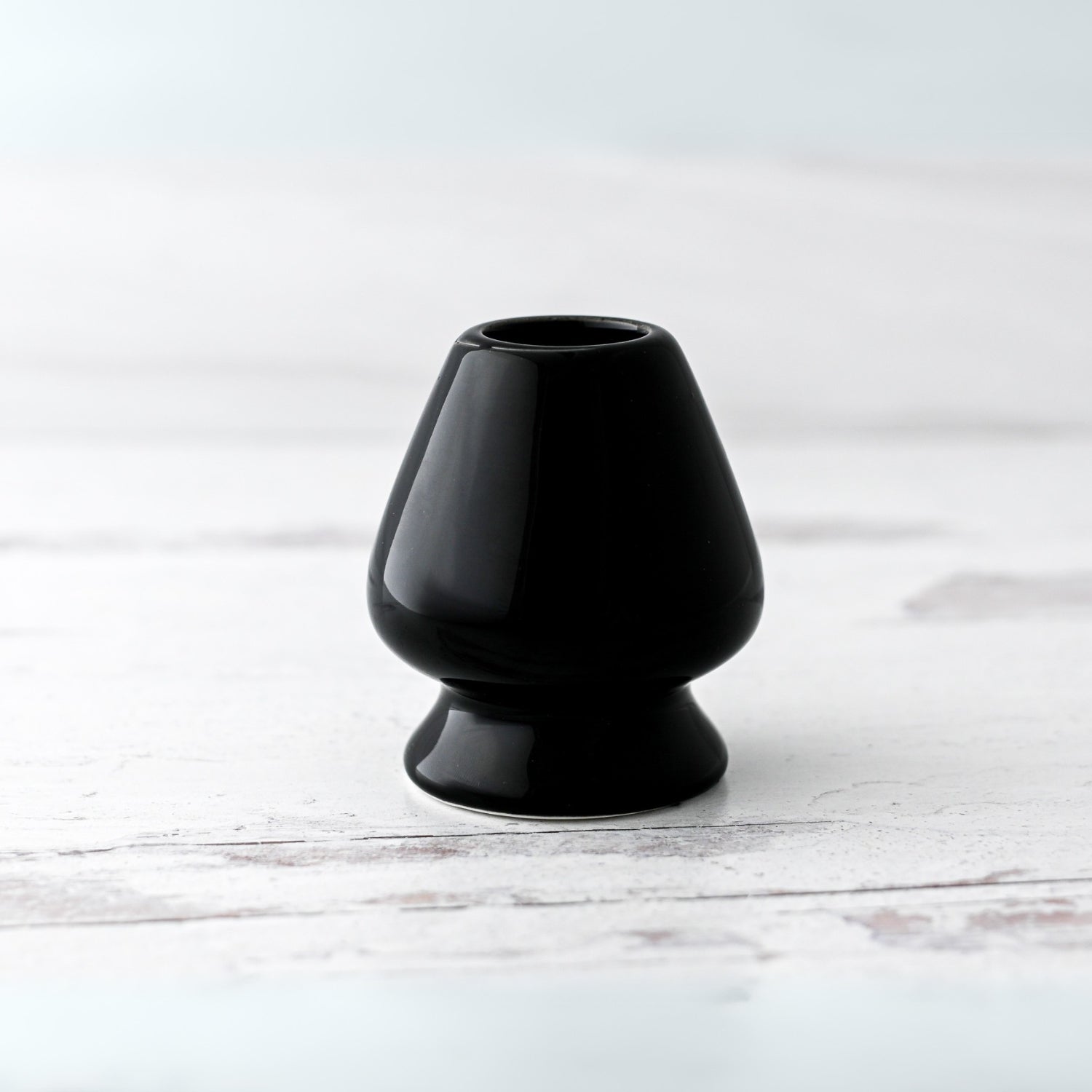 A Black Matcha Whisk Holder from the Bamboo Whisk Set, echoing a Japanese aesthetic, sits elegantly on a white wooden surface.