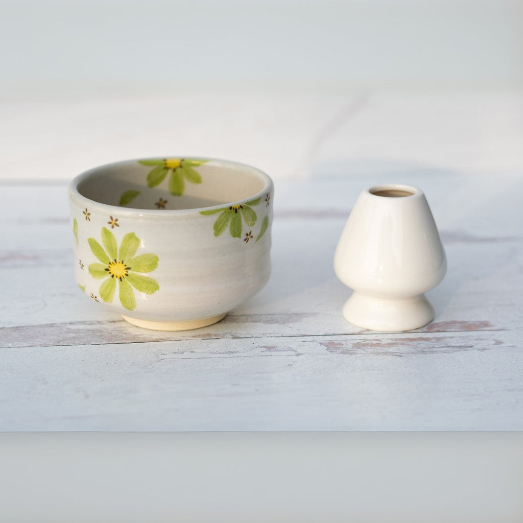 A Green Flowers Ceramic Matcha Bowl sits next to a small white egg cup on a light wooden surface.