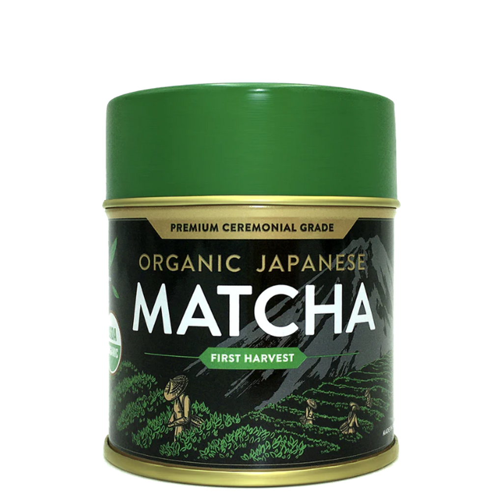 Green tin of Organic Japanese Ceremonial Grade Matcha Green Tea Powder featuring mountain and field illustrations on the label.