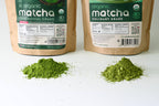 Two piles of culinary grade organic Japanese matcha powder sit before labeled Aprika Life bags of USDA & JAS certified Matcha Powder for Latte, Smoothies, and Recipes—Culinary Grade Green Tea Powder, 3.5 oz.