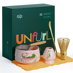 Unfurl a Pink Unfurl Matcha Gift Set featuring a whisk, strainer, scoop, Cat Print Bowl, and a stylish green box in the background.