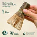 Hand holds a Dark Matcha Bamboo Whisk, crafted with 100 prongs for ceremonial Matcha tea. Eco-friendly and made from natural materials, it makes a unique gift idea.